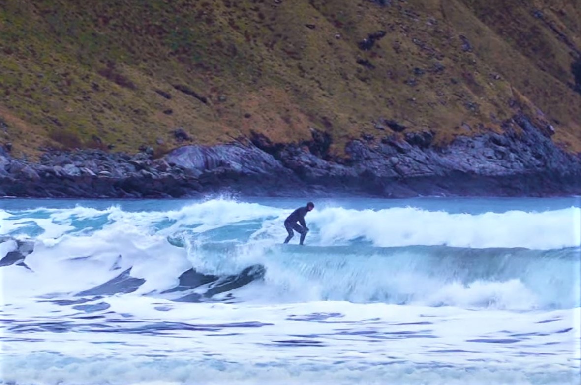 Ein person surfar i bølgene på Stadlandet, med ei skråning i bakgrunnen