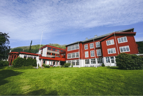 Bilde av bygget til Møre Folkehøgskule, med blå himmel og raudt bygg.