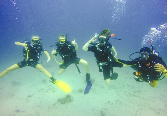 Undervannsbilde av fire dykkere som poserer for kamera ved havbunnen